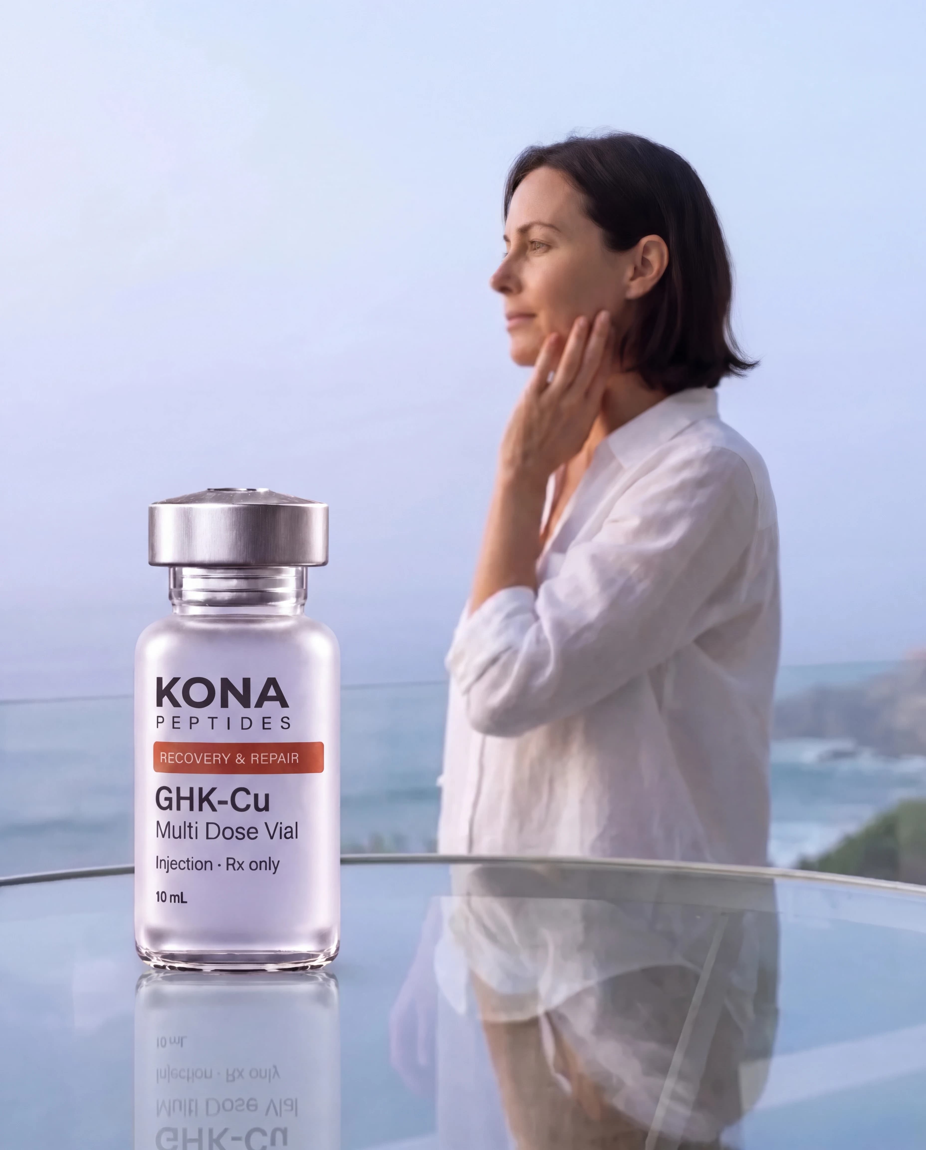 A GHK-Cu vial in front of a woman touching her jawline on a seaside balcony